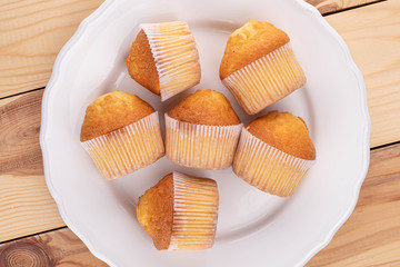 Group of six whole small baked muffin on white plate on wood