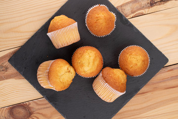 Group of six whole small baked muffin on stone on wood