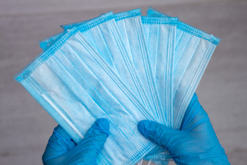 Hands wearing blue medical latex gloves hold several disposable protective medical masks, close-up, top view. Coronavirus pandemic concept