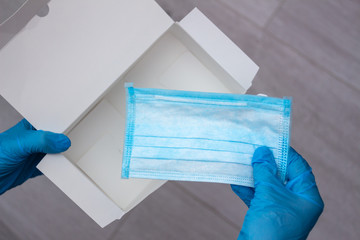 Hands wearing blue medical latex gloves hold an empty box and the last disposable protective medical mask, close-up, top view. Coronavirus pandemic concept