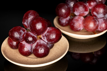 Lot of whole fresh red globe grape on two plates isolated on black glass