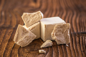cube of fresh yeast whole and crumbled on a old vintage wood board background 