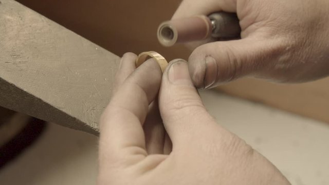 Hands of the jeweler polishes ring with the polishing machine. Goldsmith working on his workbench