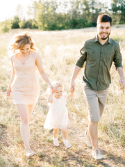 Happy young family of three smiling while spending free time outdoors. Happy loving family walking outdoor in the light of sunset. Father, mother and daughter.