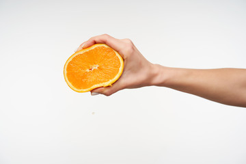Raised young fair-skinned pretty female's hand keeping half of orange and pressing it with fingers...