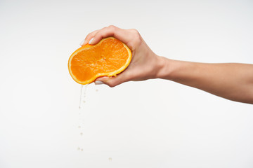 Indoor photo of young female's hand holding fresh orange and clenching it with fingers, preparing juice for breakfast, isolated against white background