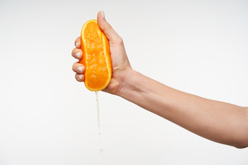 Studio shot of pretty young lady's hand keeping orange in raised hand while making fresh juice for breakfast, isolated against white background