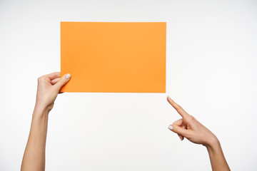 Raised young lady's hand keeping craft envelope and showing on it with forefinger while being isolated against white background. Human hands and gesturing concept