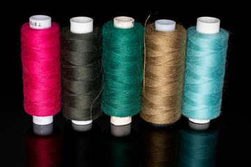 Group of five whole thread spools isolated on black glass