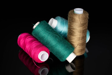 Group of four whole thread spools isolated on black glass