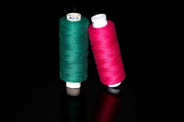 Group of two whole thread spools pink and green isolated on black glass