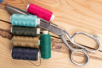 Fototapeta na wymiar Sewing scissors with thread spools on wood