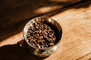 Coffee dripper with roasted coffee bean against  the sunlight in the morning. Top view of coffee dripper with roasted coffee bean on wooden background.
