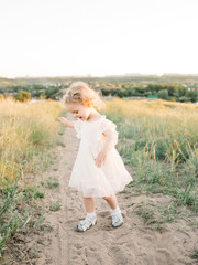 Fototapeta na wymiar Cute kid girl with bunch of wild flowers walking on a summer meadow on beautiful summer sunset. Happy child. childhood. Outdoors, at sunset on a warm evening summer. backdrop of a sunset.