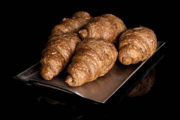 Group of five whole baked wholegrain croissant on tray isolated on black glass