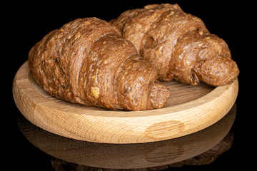 Group of two whole baked wholegrain croissant on wooden plate isolated on black glass