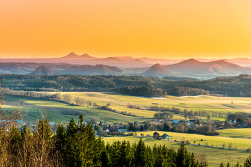 Hilly landscape illuminated by evening sunset. Green grass fields and hills on the horizont. Vivid spring rural countryside, Czech Republic