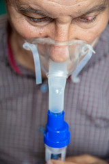 Senior man using medical equipment for inhalation with respiratory mask, nebulizer