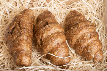 Group of three whole baked wholegrain croissant on straw mat