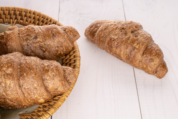 Group of three whole baked wholegrain croissant on plate with braided edge on white wood
