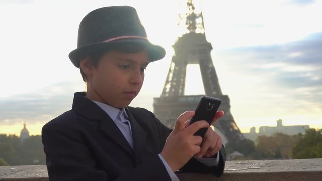 Handsome teenage boy in a hat is texting a message on the phone on the background of the Eiffel tower at the dawn, Paris, France