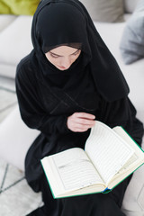 young muslim woman reading Quran at home