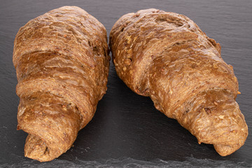 Group of two whole baked wholegrain croissant on grey stone