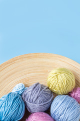 Funny multicolored woolen balls in wooden bowl on blue background. Top view. Close up. Knitting as hobby. Copy space. Vertical format.