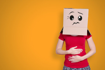 Person with cardboard box on its head and an expectant face expression holding ist belly on orange...