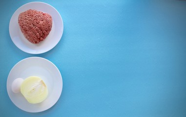 isolated white plates with minced meat, onion and egg  on a blue background