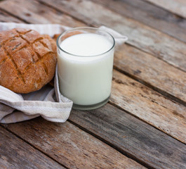 Glass of fresh organic milk and round brown rye fletbread on a rustic wooden table. Kefir, milk or Turkish Ayran drink. Space for text
