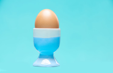 A soft-boiled egg in a cradle against a blue background in the studio