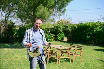 Mature senior man using a broken trimmer to trim the grass in his garden during a spring sunny day