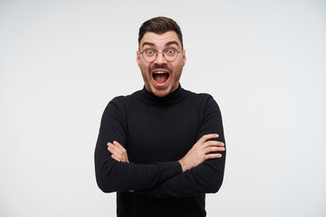 Excited young lovely bearded brunette male crossing arms on his chest and looking amazedly at...