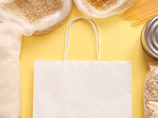 Dry goods, stockpiling, food supplies for staying home concept, delivery, donation, volunteer. Preserves, pasta, oatmeal, rice, sugar, shopping bag mockup on yellow background, copyspace, mock up