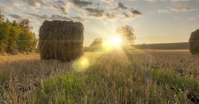 Flat hill meadow timelapse at the summer sunset time. Wild nature and rural haystacks on grass field. Sun rays and green trees. Motorised dolly slider