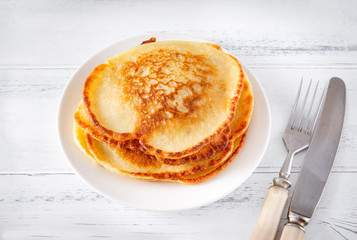 fried pancakes on a white plate, fork, knife on a white wooden background