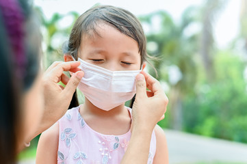 Mother is wearing a medical mask for little girl protect herself from Coronavirus when child leave the house mom is wearing mask on her nose for safety outdoor activity,illness or Air pollution
