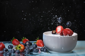 Milk splash close up of falling berries in a grey plate of milk. Blueberries and Strawberries  multivitamin cocktail. Healthy diet. Organic food. Black background.