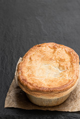Homemade flaky pasty with steak and ale gravy filling on black stone background