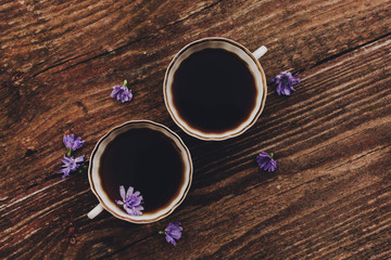 Lilac chicory flowers and cups on wooden table.