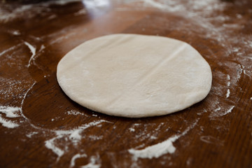 round dough lies on a wooden table sprinkled with flour,pizza dough,smoothed dough is preparing to make dumplings