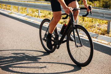 Close up of cyclist legs in sport clothing and sneakers actively riding professional bike on paved road. Mature man enjoying hobby on fresh air.