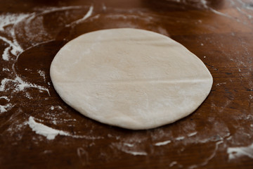 round dough lies on a wooden table sprinkled with flour,pizza dough,smoothed dough is preparing to make dumplings