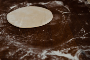 round dough lies on a wooden table sprinkled with flour,pizza dough,smoothed dough is preparing to make dumplings