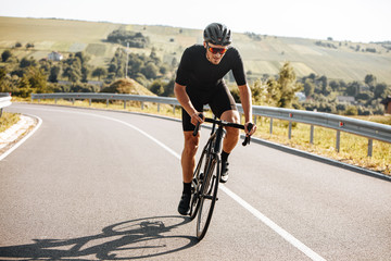 Athletic bearded man in active clothing, black helmet and mirrored glasses riding black bike with...
