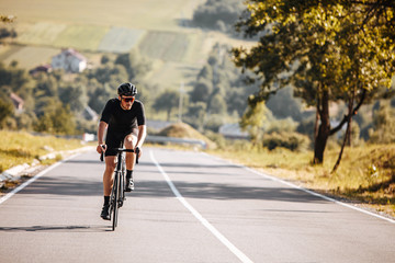 Front view of bearded man with athletic body shape in protective helmet and glasses riding bicycle with beautiful nature around. Concept of self discipline and motivation.