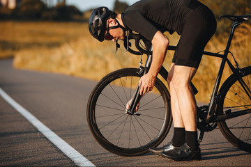 Side view of active man in sport clothing standing bent near black bike to fix wheel. Mature...