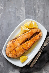 fried salmon with lemon on white dish on ceramic background