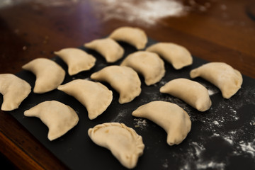 Uncooked russian vareniki on cutting wooden board with flour on baking paper. Process of making vareniki. top view.Typical Eastern European food, called dumplings, dumplings, dumplings, pies or pies